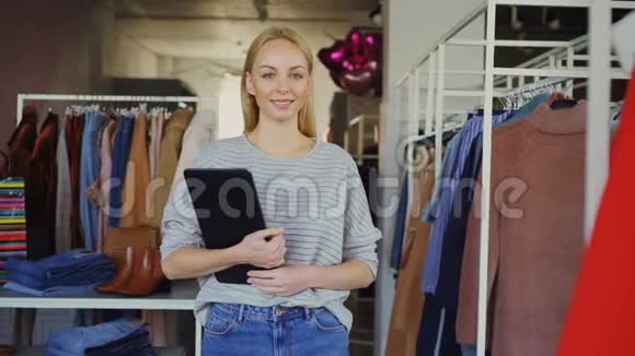 成功的年轻女商人站在她的服装店里拿着平板电脑微笑着看着相机的画像视频的预览图