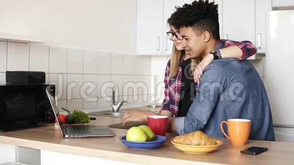 可爱的两个年轻人拥抱和使用笔记本电脑在厨房上网青年关系生活视频的预览图