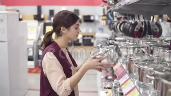 年轻的女性消费者在电器商店里从各种厨具中选择炊具检查全钢视频的预览图