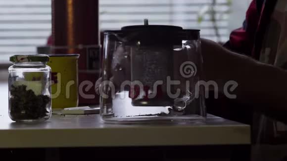 盖伊在桌子上用大杯子和玻璃茶壶做卷烟视频的预览图