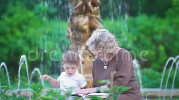 奶奶和小孙子在公园的喷泉边看书视频的预览图