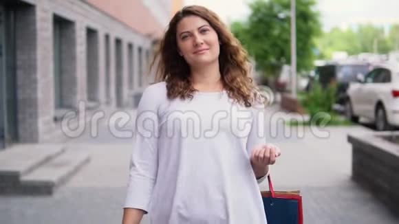 一个穿着浅色连衣裙留着长发的女孩在购物后手里拿着包裹慢动作视频的预览图