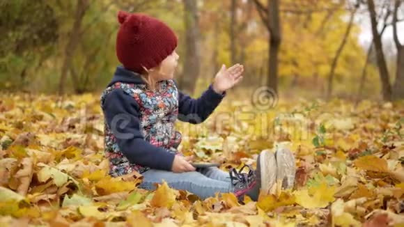 女孩坐在秋天的黄叶里带着电话视频的预览图