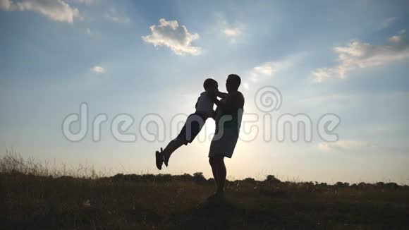 在一个阳光明媚的日子里父亲在草地上旋转他的小儿子爸爸在大自然中旋转婴儿家庭在球场上打球视频的预览图