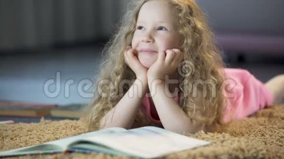 可爱的女孩梦想着幸福的未来躺在家里柔软的地毯上视频的预览图