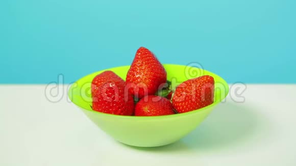 浆果红色成熟草莓在绿色碗在蓝色背景视频的预览图