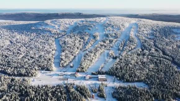 观看现代滑雪基地和滑雪道周围的森林在冬季与蓝天录像空中景观视频的预览图