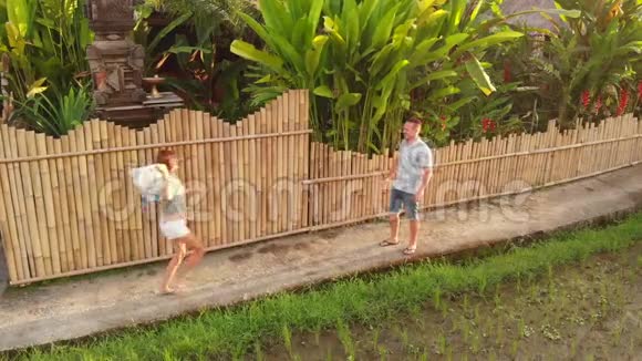 4K航天无人机拍摄的画面显示年轻夫妇在日落时分靠近豪华别墅的稻田旋转和拥抱视频的预览图