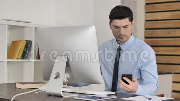 年轻商人在电脑工作时使用智能手机视频的预览图