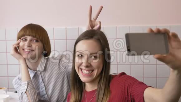 两个年轻的高加索美女坐在咖啡馆里自拍笑笑做滑稽的脸女朋友朋友视频的预览图