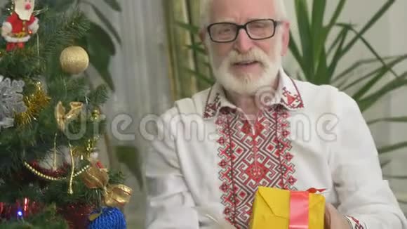戴眼镜的可爱老人在圣诞树附近拿着圣诞礼物视频的预览图