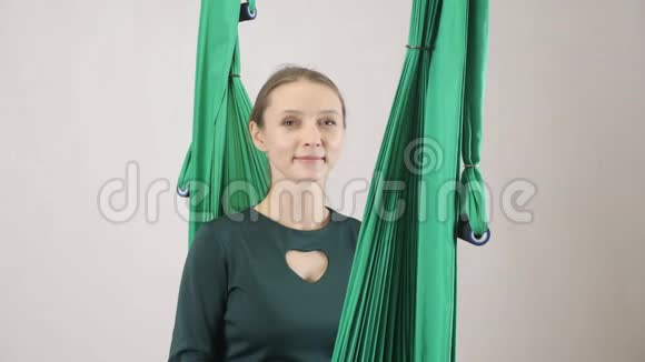 年轻的女人坐在吊床上微笑着用摇头说是空中航空飞行健身教练训练冥想视频的预览图