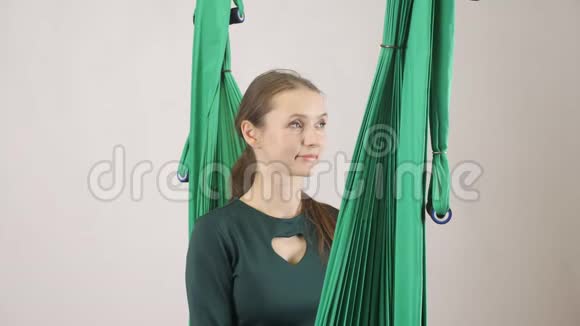 年轻的女人坐在吊床上微笑的女人展示你叫我标志空中航空飞行健身教练训练冥想视频的预览图