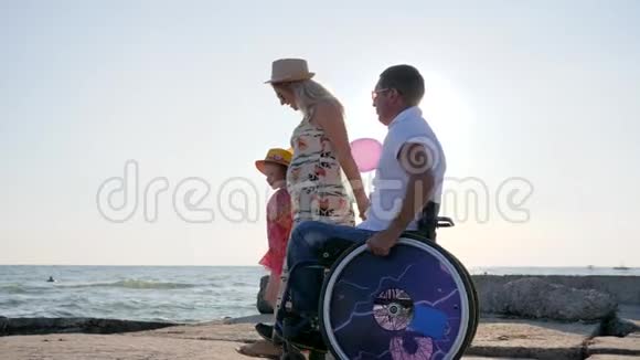 快乐的残疾人爸爸和家人一起走在海边背光孩子带着五颜六色的气球走视频的预览图