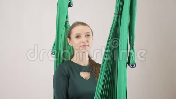 年轻的女人坐在吊床上微笑的女人展示着手掌的标志空中航空飞行健身教练训练冥想视频的预览图
