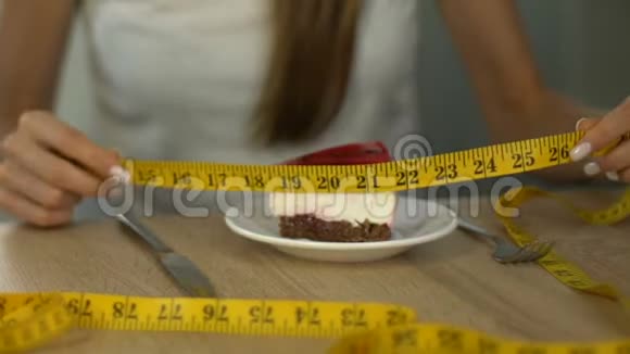 苗条的女孩用胶带线测量蛋糕在饮食中计算卡路里的概念视频的预览图