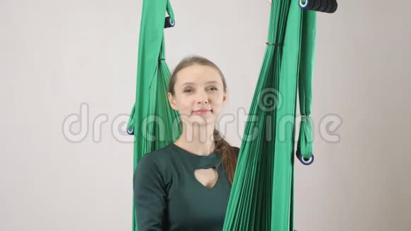 年轻的女人坐在吊床上微笑并发出一个空气亲吻空中航空飞行健身教练训练冥想和谐视频的预览图