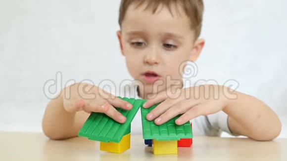 一个孩子正在玩彩色积木盖房子坐在白色背景的桌子旁特写慢慢地视频的预览图