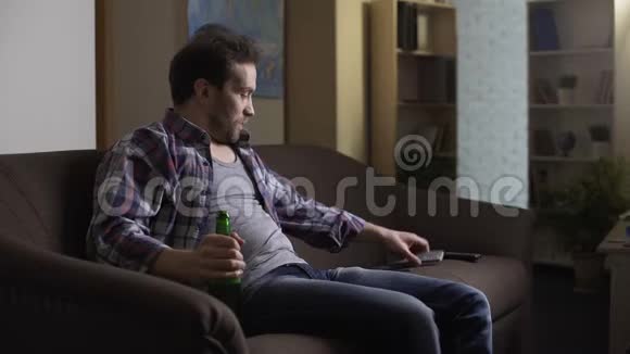 坐在沙发上的人手里拿着啤酒瓶用遥控器开关电视视频的预览图