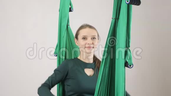年轻的女人坐在吊床上微笑着高兴地看着相机空中航空飞行健身教练训练视频的预览图