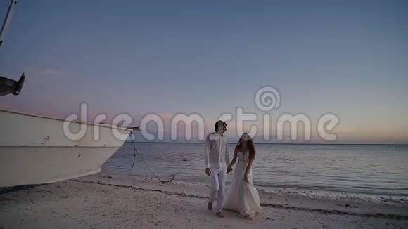 新娘和新郎新婚夫妇在海边的热带海滩上在日落时散步他们是在视频的预览图