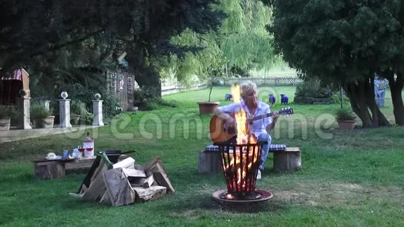 坐在篝火旁弹原声吉他的年轻女子视频的预览图