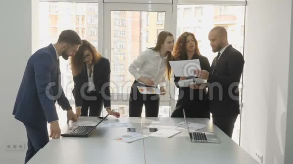 办公室工作人员两名年轻男子和三名年轻妇女站在桌边打开电脑拿着文件视频的预览图