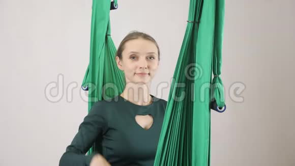 年轻的女人坐在吊床上微笑着挥手打招呼你好嗨航空飞行健身视频的预览图