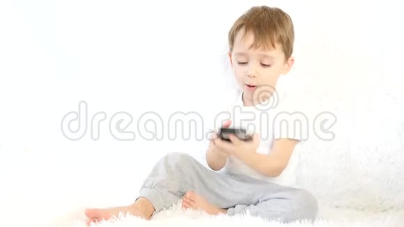 一个孩子坐在白色的沙发上玩着智能手机微笑着运动相机滑块视频的预览图