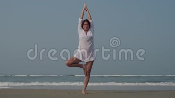 年轻女子在海洋附近练习树瑜伽姿势4K视频的预览图