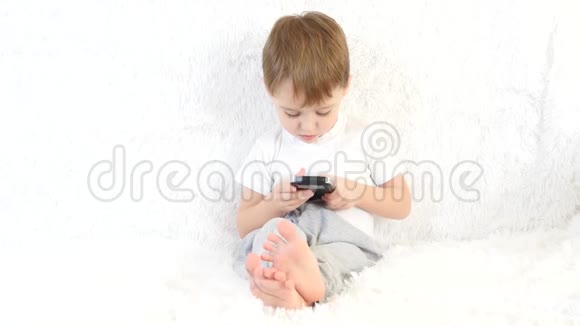 小男孩坐在白色沙发上喜欢玩智能手机视频的预览图