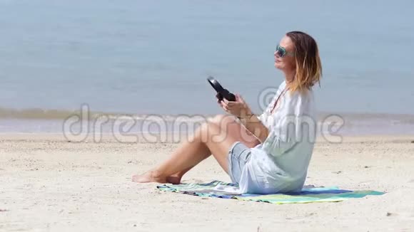 一个年轻的女人在阳光明媚的日子里在海滩上听音乐视频的预览图