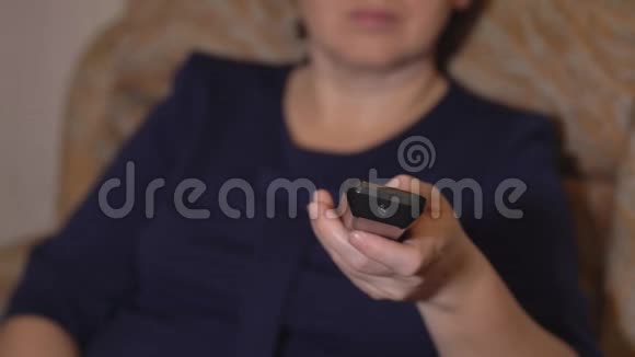 在一个穿蓝色衣服的女人的背景上用遥控器特写一只女性的手视频的预览图
