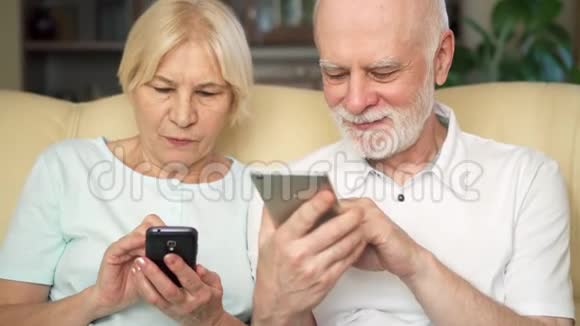 老两口坐在家里的沙发上现代养老金领取者使用移动浏览阅读新闻视频的预览图