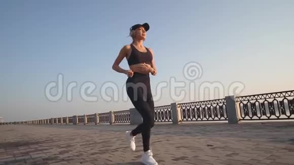 慢镜头拍摄一个纤细的金发女郎听着耳机里的音乐沿着海滨奔跑视频的预览图