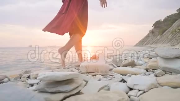 在日落时分一个穿着红色裙子在风中飘舞的赤脚女孩的腿后特写慢动作视频的预览图