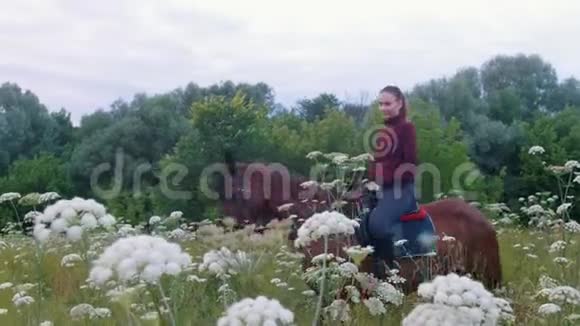 骑马的年轻女骑手带着鲜花在田野里散步视频的预览图