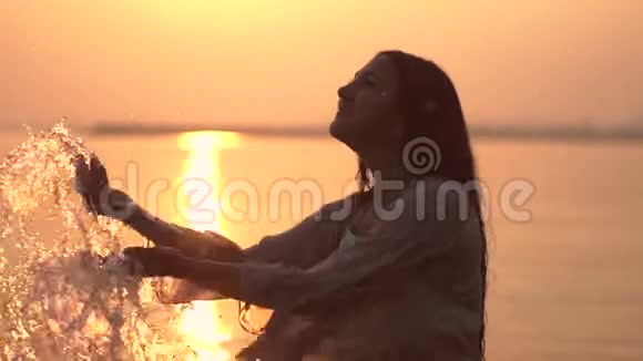 迷人的年轻女孩在阳光的映衬下双手在水中飞溅慢动作视频的预览图