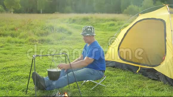 一个人靠近火边的帐篷看着一个沸腾的锅视频的预览图