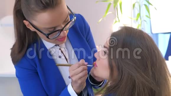 化妆师在美容院将口红用刷子涂在模特女孩的嘴唇上视频的预览图