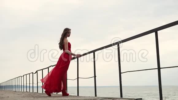 穿着长裙的女人紧紧抓住靠近大海的栏杆风吹着头发视频的预览图