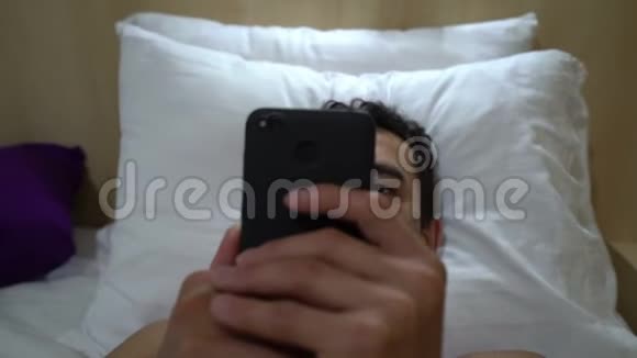 男人在床上放松在智能手机上阅读近距离稳定射击休闲活动跟踪射击手机视频的预览图