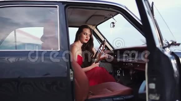 一位身穿红色连衣裙的美女坐在一辆罕见的复古车后面视频的预览图
