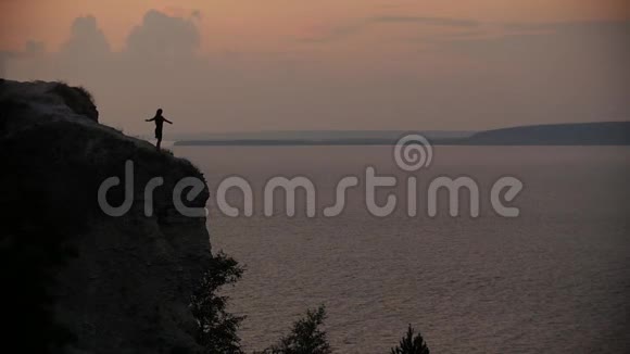 日落时分穿着黑色裙子的女性剪影在海边的悬崖边翩翩起舞视频的预览图