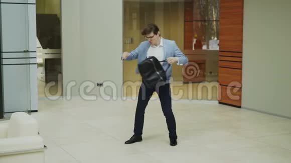 疯狂的商人在现代大厅里拿着公文包跳舞而他的同事们在散步看着他惊讶视频的预览图