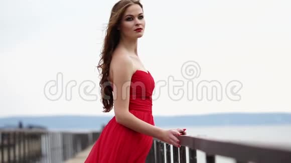 一位漂亮的女士喜欢风吹拂着她鲜红的长裙和卷发视频的预览图