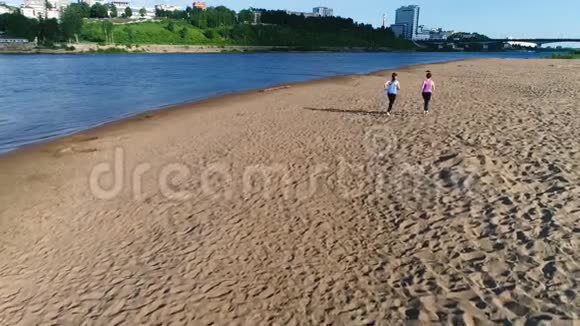 日落时两个女人沿着河沙滩慢跑美丽的城市景色视频的预览图