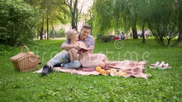 可爱的一对情侣在野餐浪漫的约会中舒适地坐在地毯上讨论书视频的预览图