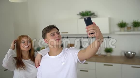 漂亮的年轻夫妇在厨房的家里在智能手机上做自拍年轻的男人和女人视频的预览图