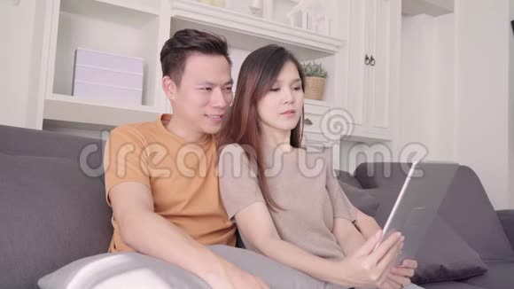 亚洲夫妇使用平板电脑视频电话与朋友在客厅在家里视频的预览图
